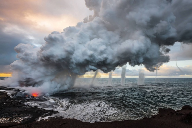 Lava from Kilauea volcano is poured into the sea, creating a huge escape of steam. As it rose, multiple vortices began spinning off of the huge plume. Hawaii.
