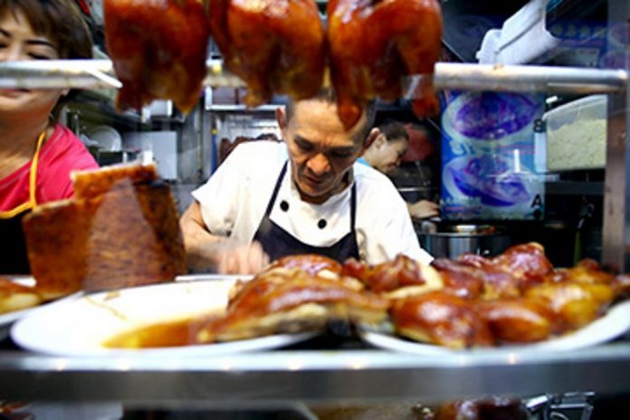 chan hon meng is chopping the chicken in his small local street food vendor