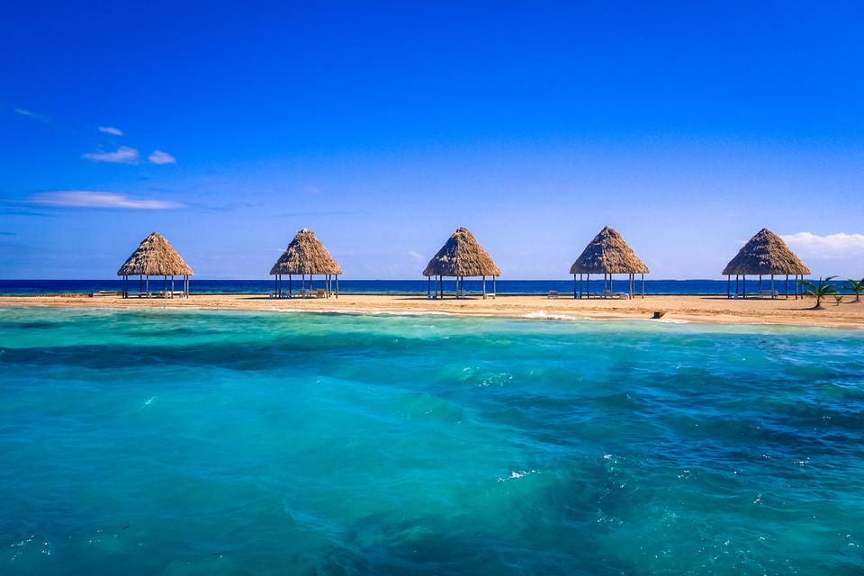 A row of thatched palapas on golden sand on the tiny island of Rendezvous Caye in Belize